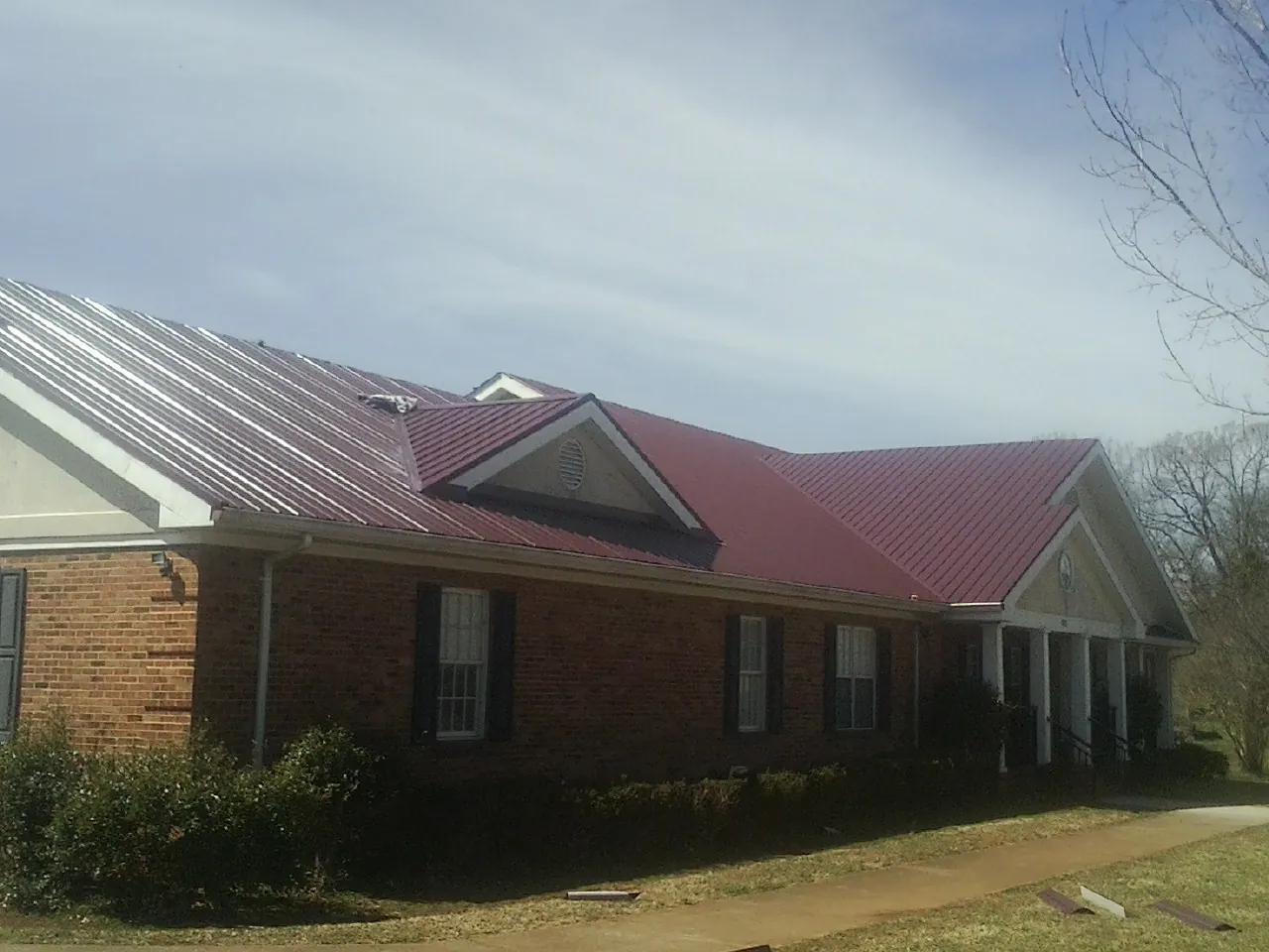 Red metal roof with gabled entries on a long brick building, from a Hail Damage Roof Repair job in Sylvania