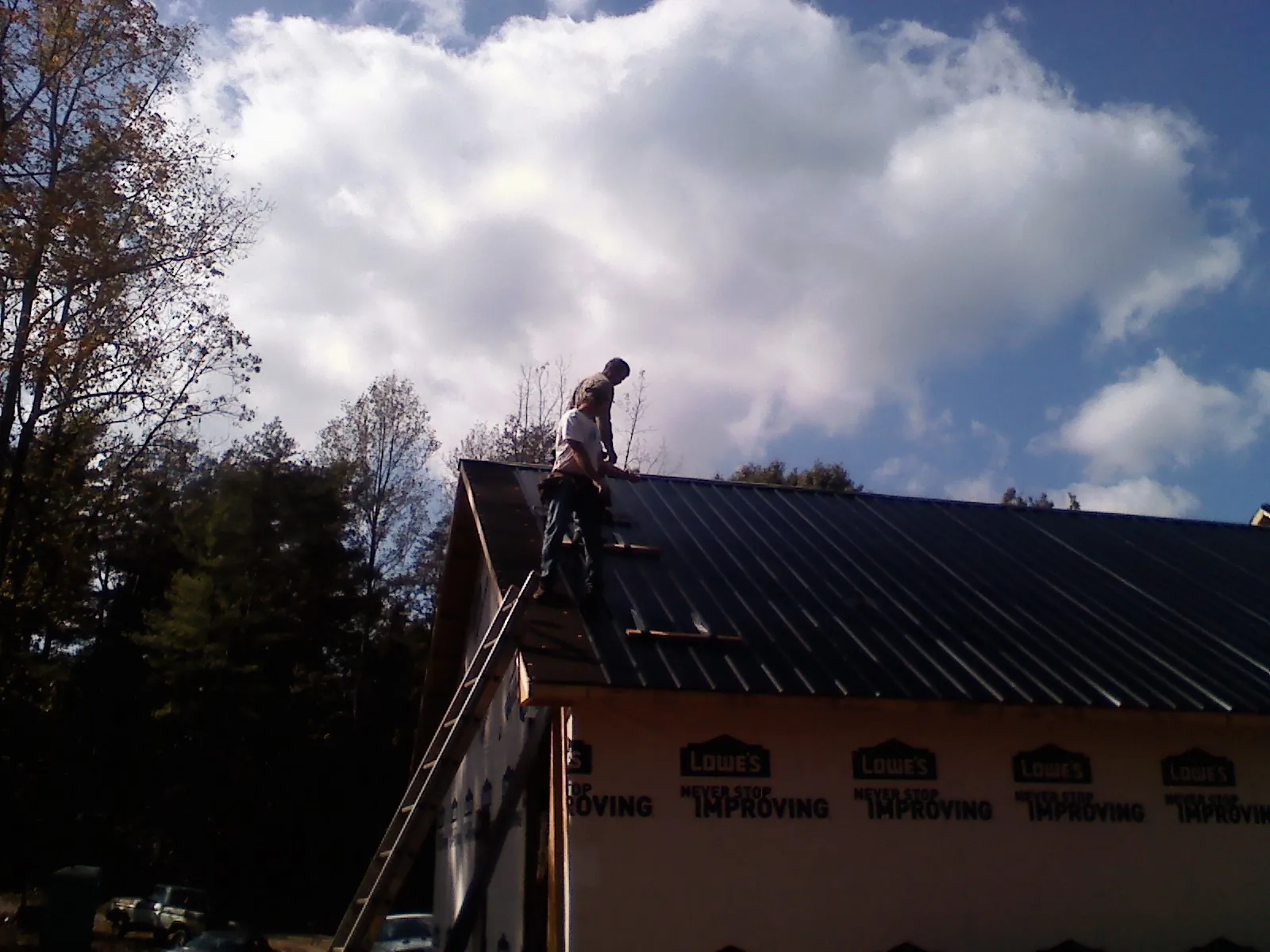 Roofer fastening dark metal panels high against a cloudy sky, from a Roof Inspection job in Sylvania